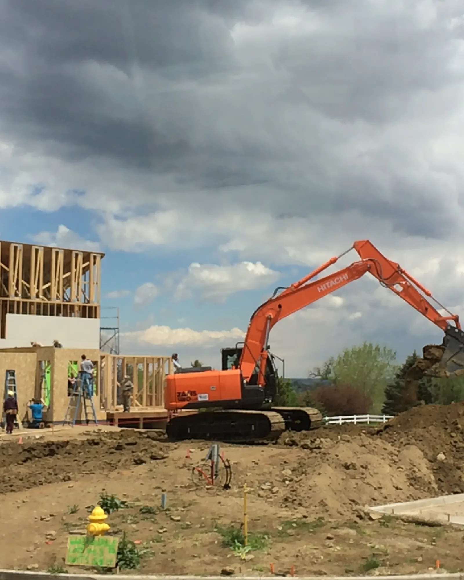 A Rudkin excavator moving earth on a Northern Colorado site with a house under framing behind it